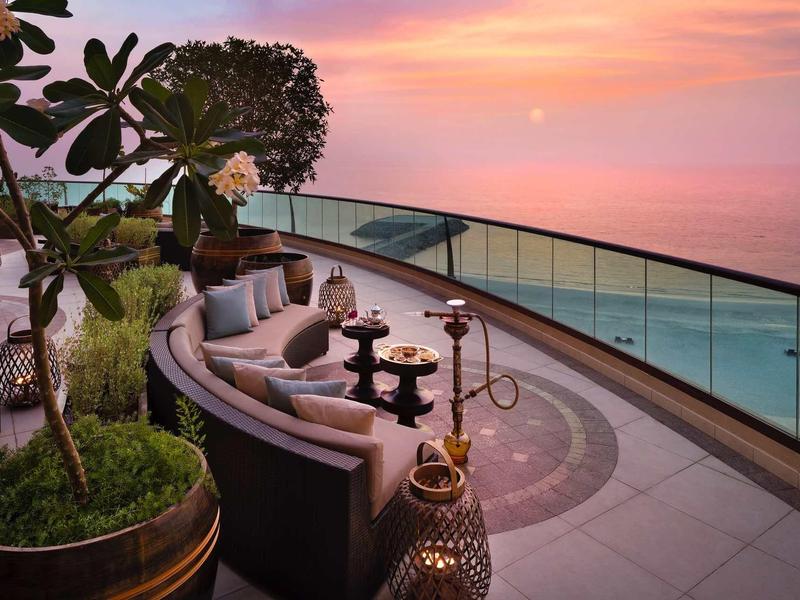 Terrassen-Lounge mit runden Sofas, Pflanzen und Blick auf Meer bei Sonnenuntergang.