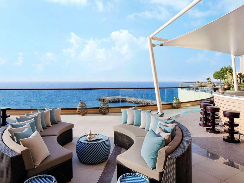 Moderner Außenbereich mit Strandblick, runden Sofas, blauen Kissen und Barhockern im Freien.