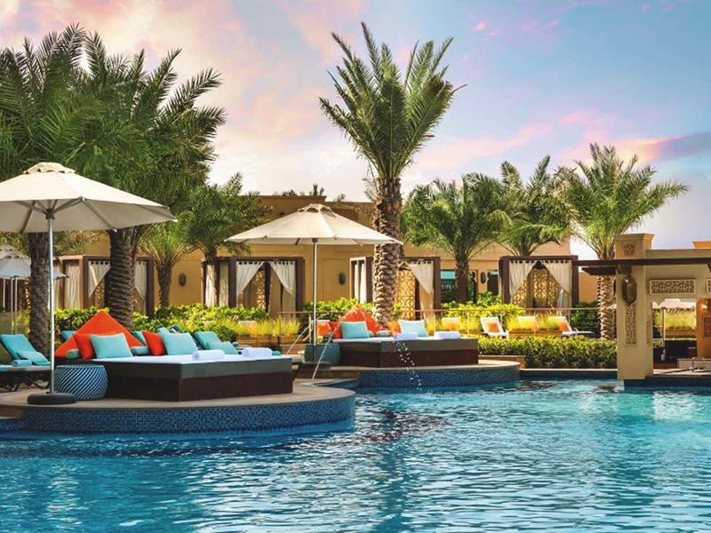 Luxuriöser Pool mit Liegen, Sonnenschirmen und Palmen bei Sonnenuntergang im Resort.