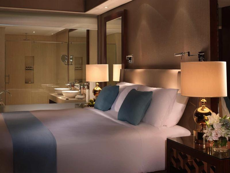 Schlafzimmer mit großem Bett, blauen Kissen, Nachttischlampen und einem durchsichtigen Badezimmer.