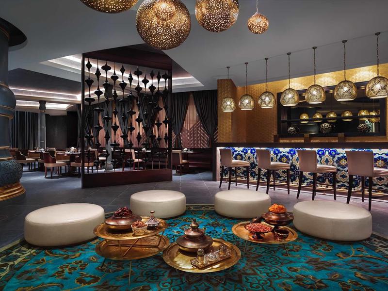 Moderner Hotellobby mit Sitzinseln, blau-grünem Teppich und goldenen Kugelpendelleuchten.