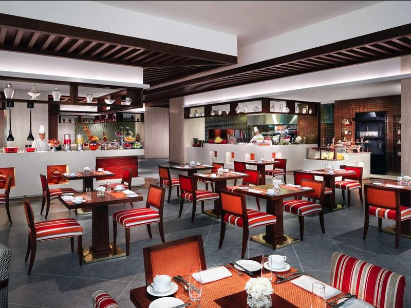 Modernes Restaurant mit roten Stühlen, Holztischen und offener Bar in warmem Ambiente.