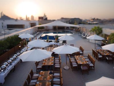 Rooftop terrace with white umbrellas, dining tables, and city view at sunset.