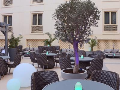 Espace extérieur moderne d'un hôtel avec tables, chaises et sphères décoratives éclairées.