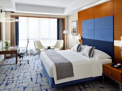 Modern hotel room with large bed, desk, chairs, and a large window with curtains.