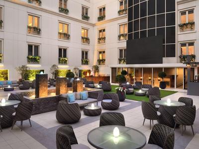 Modern hotel courtyard with round tables, bean bag chairs, and warmly lit windows.