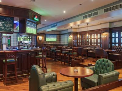 Cozy hotel bar with wooden counter, leather armchairs, and multiple seating areas.
