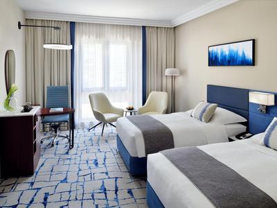 Hotel room with two beds, modern design, carpet flooring, and seating area by the window.