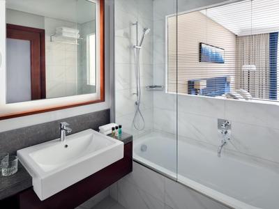 Modern hotel bathroom with white bathtub and sink, glass shower wall and mirror.