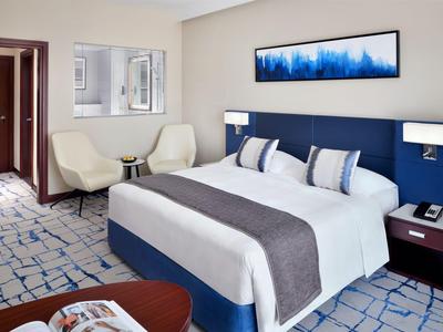 Modernly furnished hotel room with a large bed, two armchairs, and abstract wall art.