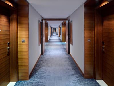 Un long couloir d'hôtel avec moquette et portes en bois des deux côtés, éclairé par des plafonniers.