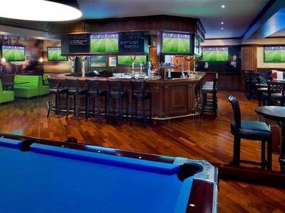 Intérieur d'un bar sportif avec table de billard, comptoir de bar et téléviseurs diffusant du sport.
