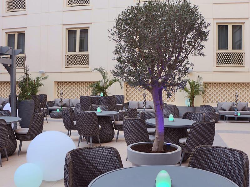 Nowoczesny teren zewnętrzny hotelu z okrągłymi stolikami, krzesłami i podświetlanymi dekoracjami.