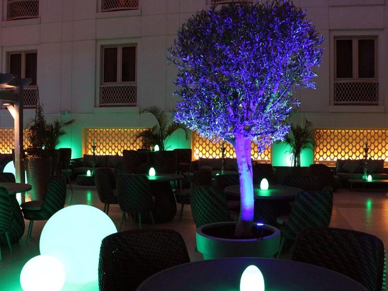 Nowoczesny taras hotelowy nocą z oświetlonymi drzewami i strefami relaksu.