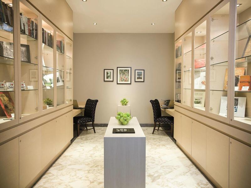 Jasne pomieszczenie z gablotami, dwoma fotelami i małym stołem z rośliną na środku.