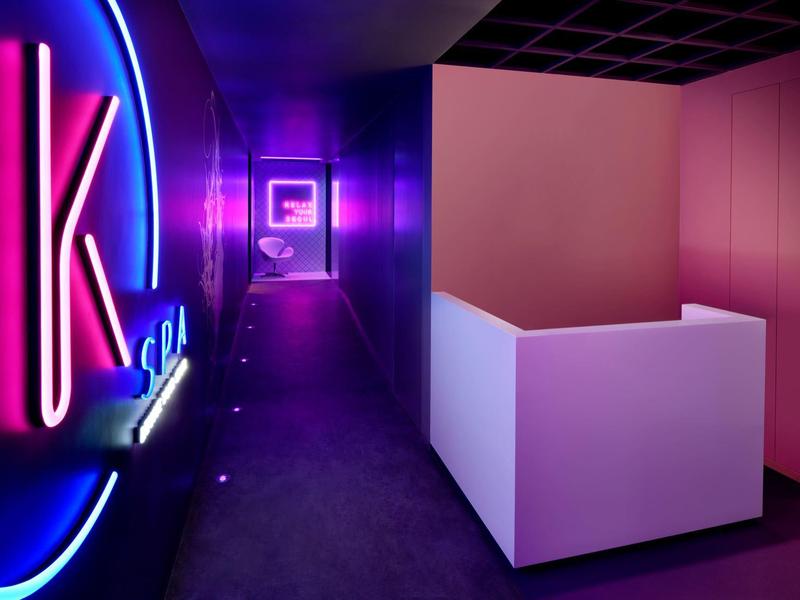 Korytarz z jasnym fioletowym i niebieskim oświetleniem neonowym w nowoczesnym wnętrzu hotelu.