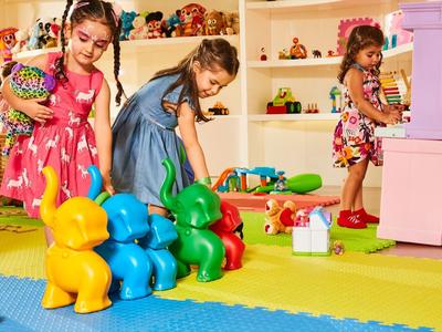 Drei Mädchen spielen in buntem Raum mit bunten Spielsachen und großen, bunten Hundefiguren.