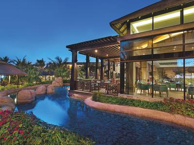 Luxuriöses Haus mit Pool, Holzterrasse und großer Glasfront bei Abenddämmerung.