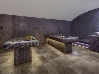 Moderner Wellnessraum mit beheizten Marmorliegen, gedämpfter Beleuchtung und Steinfliesenboden.