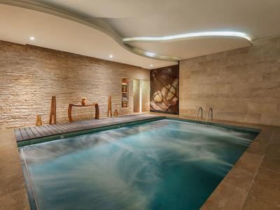 Moderner Innenpool mit Wasserwirbeln, Steinfassarben, warmem Licht und minimalistischer Holz-Dekoration.