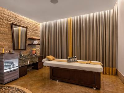 Wellnessraum mit Massageliege, gemütlicher Beleuchtung, Vorhängen und dekorativen Elementen an der Wand.