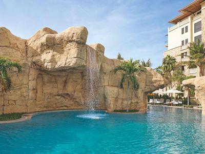 Zwembad met waterval voor hotelgebouw en palmbomen onder een heldere lucht