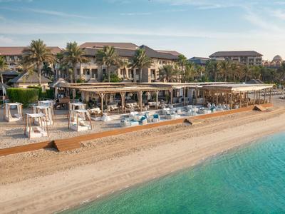 Strandhotel mit Sandstrand, Palmen und blauer Lagune unter blauem Himmel am Abend.