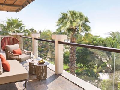 Balkon mit gemütlicher Sitzecke, Kissen und Blick auf Palmen bei sonnigem Wetter.