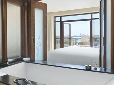 Moderner Raum mit großer Badewanne und offenem Fenster mit Blick auf ein helles Schlafzimmer.