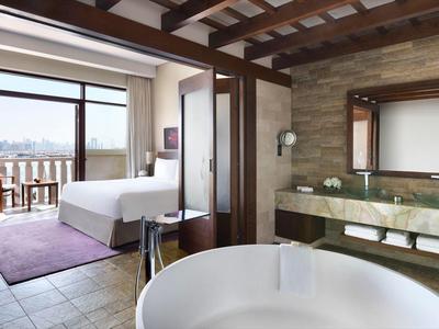 Modernes Schlafzimmer mit Balkon, großem Bett, freistehender Badewanne und Natursteinwand im Bad.