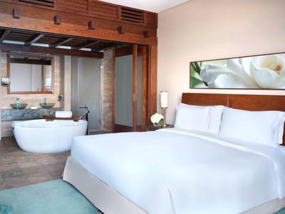 Modernes Schlafzimmer mit weißem Bett, freistehender Badewanne und Holzbalkendecke.