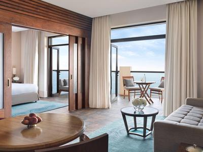 Helles Wohnzimmer mit großen Fenstern, hellen Vorhängen, Holzmöbeln und Blick auf Terrasse und Meer.