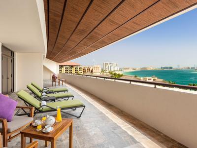 Groot balkon met ligstoelen en zeezicht in een hotelkamer.