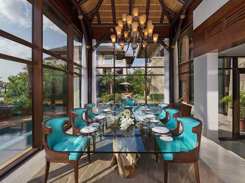 Eleganter Essbereich mit blau gepolsterten Stühlen, Glaswand und Kronleuchter in modernem Haus.