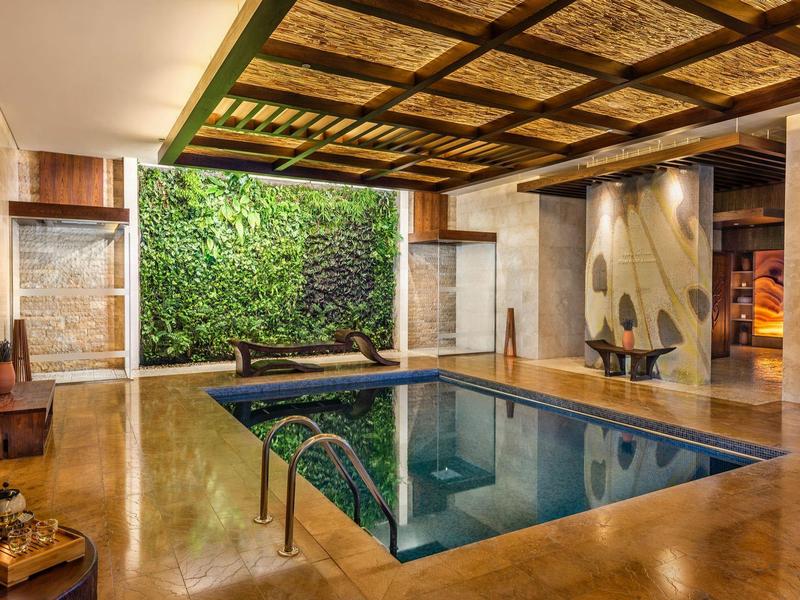 Innenraum mit quadratischem Pool, vertikaler Pflanzenwand und Holzdecke mit dekorativem Muster.