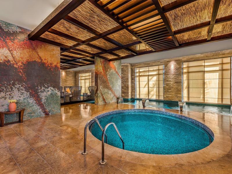 Innenbereich des Schwimmbads mit rundem Pool, warmen Farben und großen Fenstern für Tageslicht.