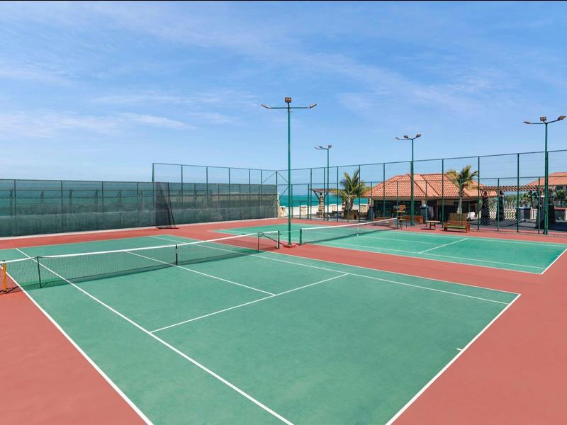 Ein leerer Tennisplatz mit grünem Spielfeld und rotem Rand bei klarem Himmel.