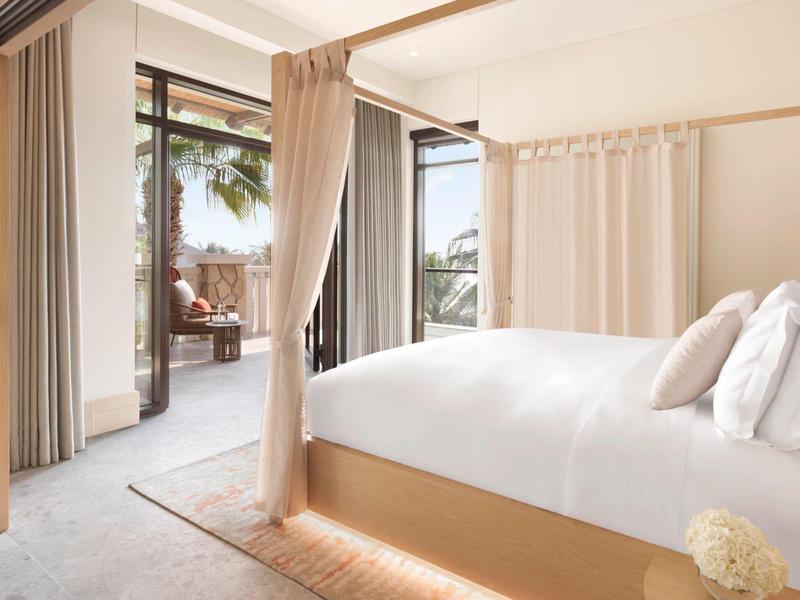 Modernes Schlafzimmer mit hellem Bett, weißen Vorhängen und Balkon mit Pflanzen draußen.