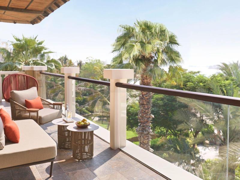 Balkon mit gemütlicher Sitzecke, Kissen und Blick auf Palmen bei sonnigem Wetter.