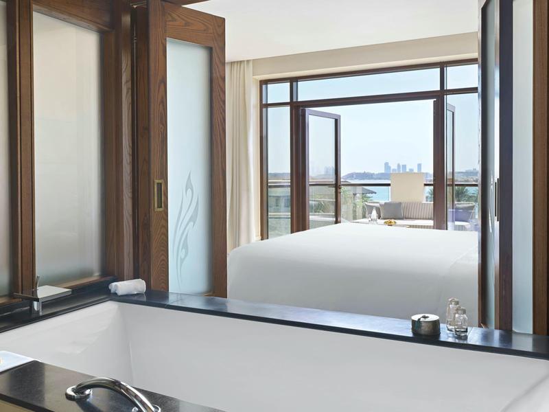 Moderner Raum mit großer Badewanne und offenem Fenster mit Blick auf ein helles Schlafzimmer.