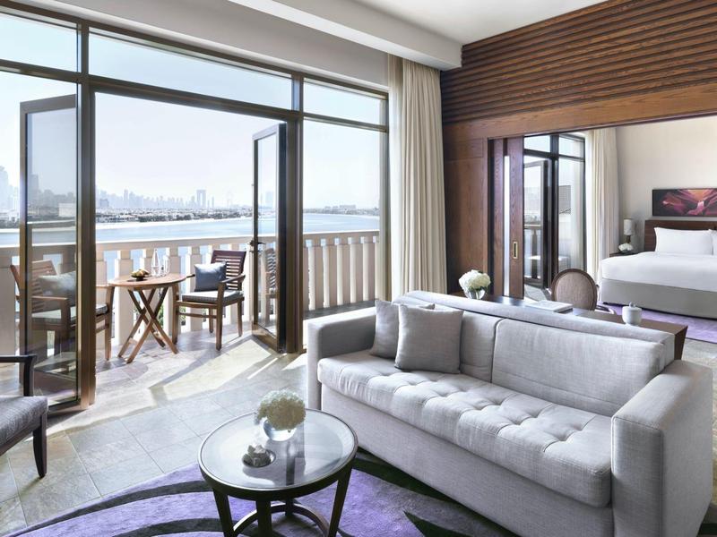 Helles Wohnzimmer mit grauem Sofa, Glastisch und Balkon mit Stadtblick bei Tageslicht.