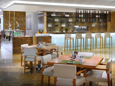 Area bar moderna in hotel con mobili in legno chiaro e bancone illuminato in atmosfera calda.