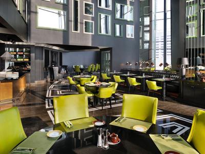 Ristorante d'hotel moderno con tavoli neri e sedie verdi in una stanza luminosa e spaziosa.