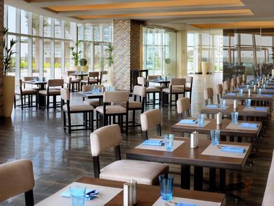 Ristorante moderno con pavimenti in legno, tavoli, sedie e grandi finestre che lasciano entrare luce naturale.