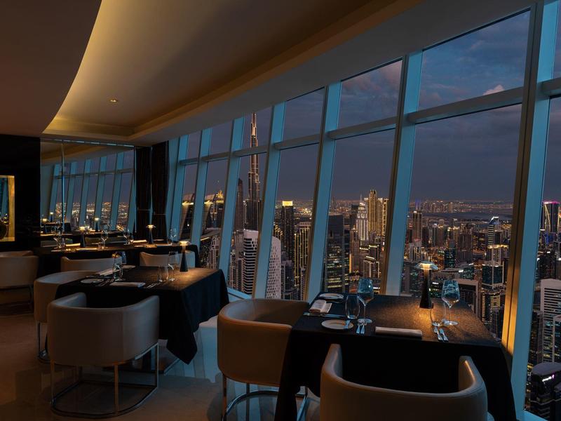 Elegancka restauracja na wysokości z panoramicznymi oknami i nocnym widokiem na miasto.