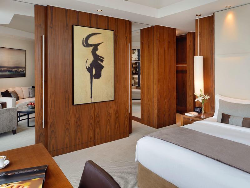 Elegancki pokój hotelowy z łóżkiem podwójnym, fotelami i ciepłym drewnianym wystrojem.