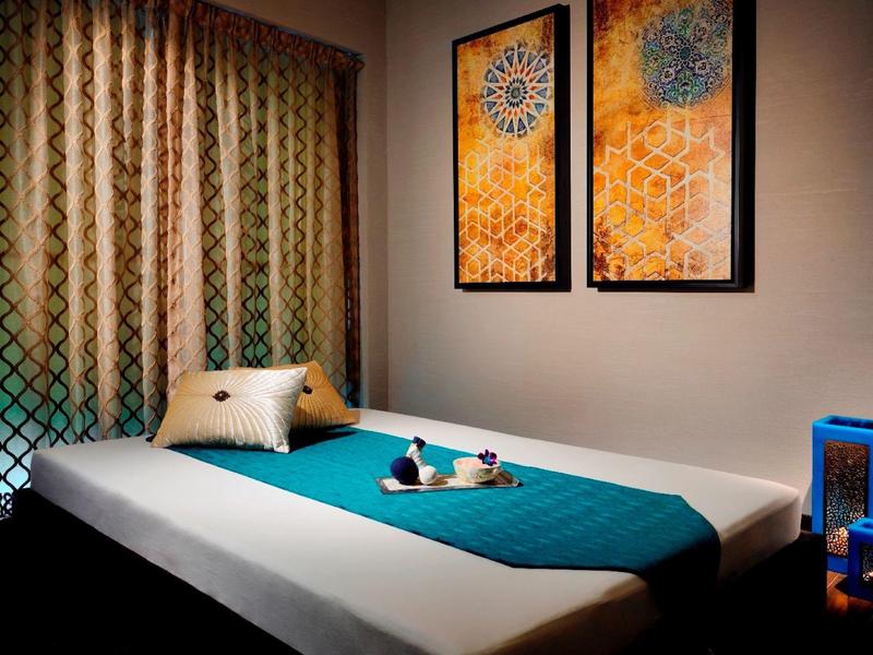 Przytulny pokój hotelowy z prostym łóżkiem, turkusowym kocem i nowoczesną sztuką na ścianie.