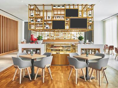 Moderní restaurace s dřevěnou podlahou, šedými židlemi a barem s visícími policemi.