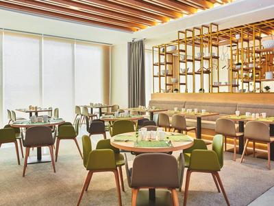 Modern hotel restaurant with green chairs and large windows letting in natural light.