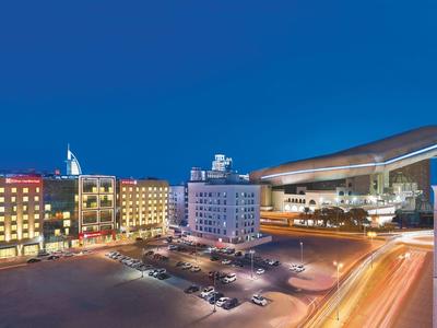 Illuminated hotel and event hall at night with parking lot and clear blue sky.